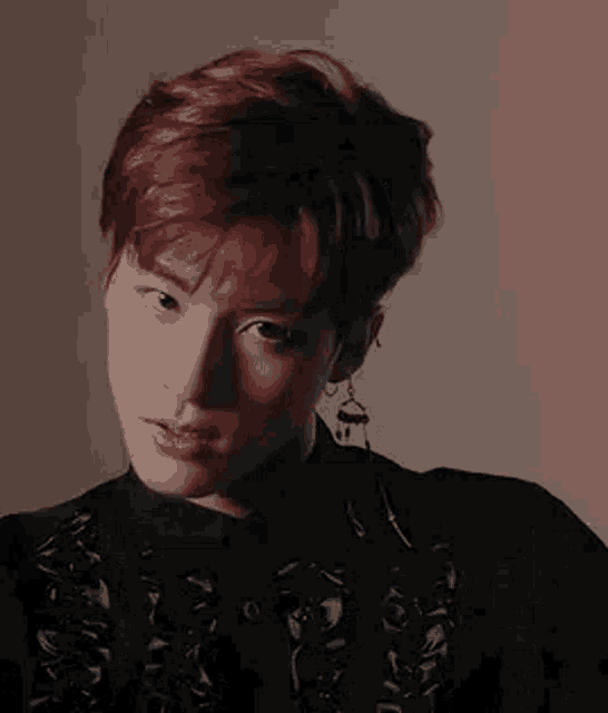 a close up of a young man with red hair wearing earrings and a black shirt .