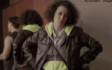 a woman in a leather jacket and neon yellow hoodie is standing with her hands on her hips .