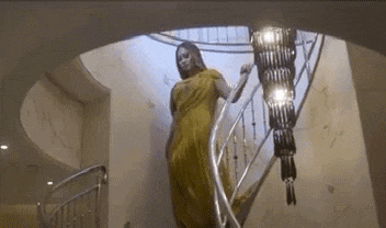 a woman in a yellow dress is walking down a spiral staircase in a house .
