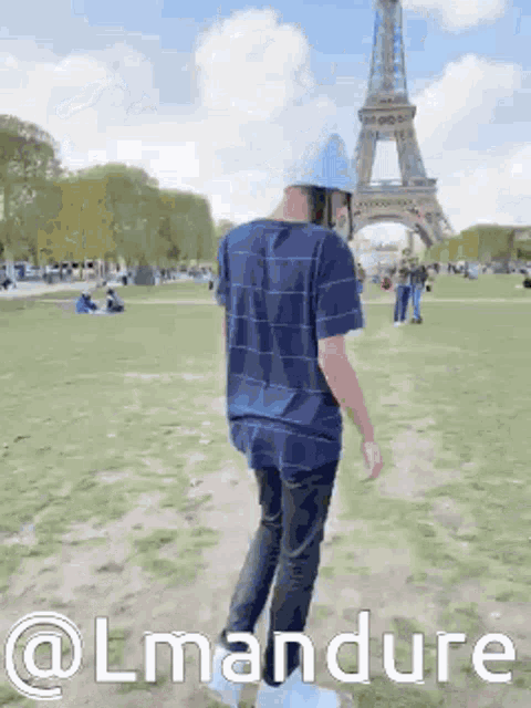 a man in a blue shirt is walking in front of the eiffel tower