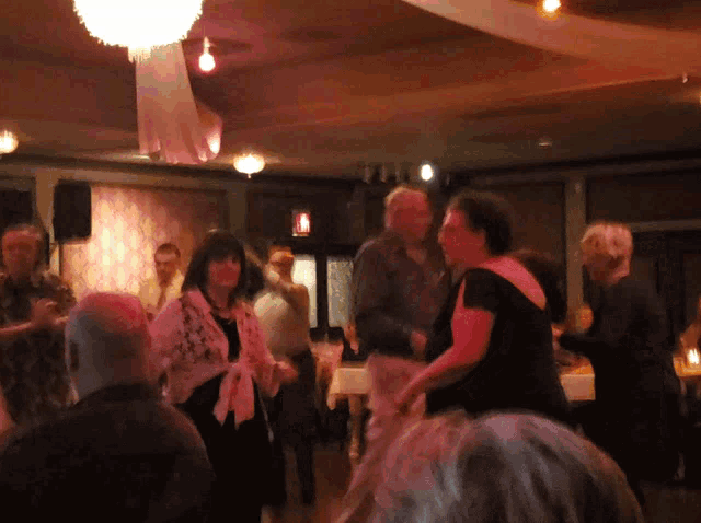 a group of people are dancing in a room with a red exit sign in the background
