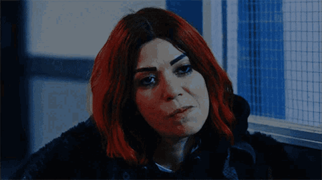 a woman with red hair is looking at the camera with a serious look on her face