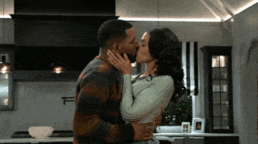 a man and woman kissing in a kitchen in front of a stove