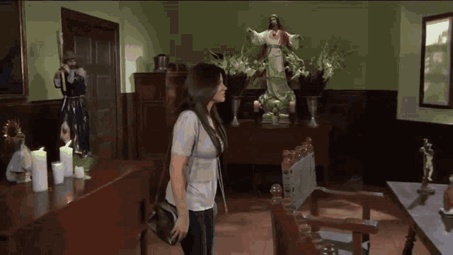 a woman stands in front of a statue of jesus in a room with candles