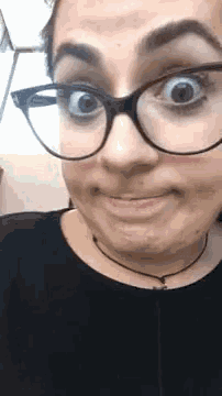 a woman wearing glasses and a black shirt is making a face .