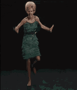 a woman in a green dress is dancing with her hands in the air
