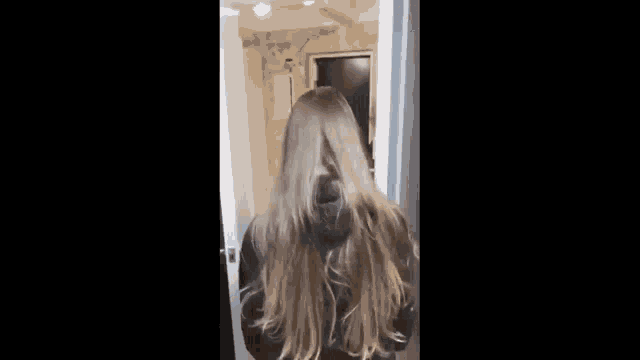 a woman with long hair is standing in front of a door in a hallway .