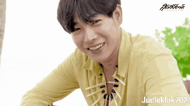 a young man wearing a yellow shirt and a necklace is smiling