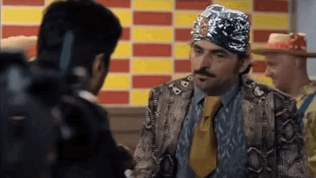 a man in a snakeskin jacket and tie is talking to another man in a restaurant .