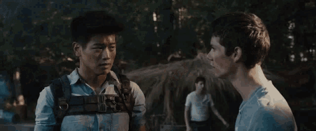 two men are standing next to each other in a forest and talking .