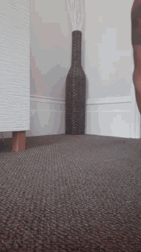 a wicker vase sits on a brown carpet next to a white wall