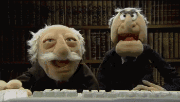 two muppets are looking at a keyboard in front of bookshelves