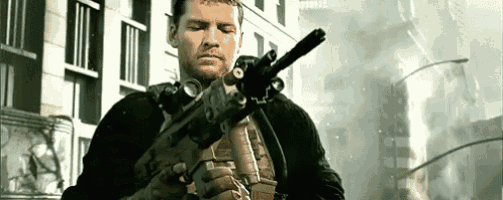 a man in a black jacket is holding a rifle in front of a building .