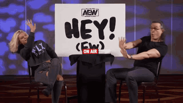 a man and a woman sitting in front of a sign that says hey