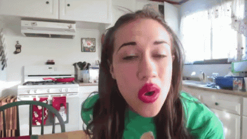 a woman with red lipstick on her lips is sitting in a kitchen