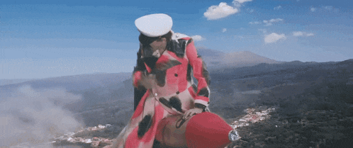 a woman in a red coat and white hat is standing on top of a mountain