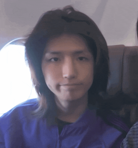 a man with long hair wearing a purple jacket looks at the camera