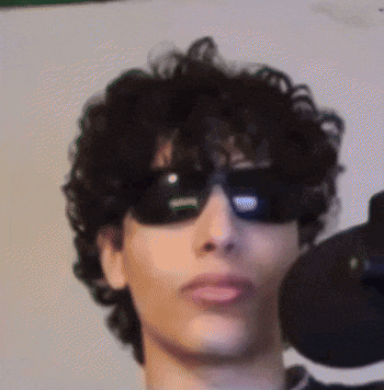 a man with curly hair wearing sunglasses and a microphone .
