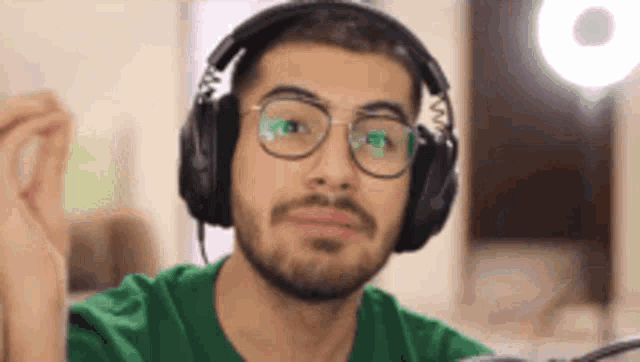 a man with a beard wearing headphones and glasses is looking at the camera .