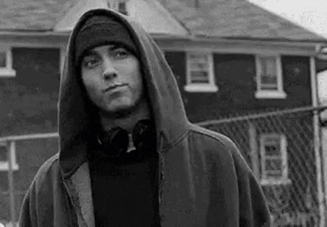 a black and white photo of a man wearing a hooded jacket and a beanie .