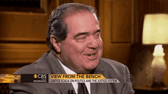 a man in a suit and tie is sitting in front of a cbs screen