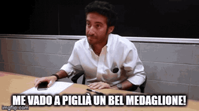 a man sitting at a table with the words me vado a piglia un bel medaglione written below him