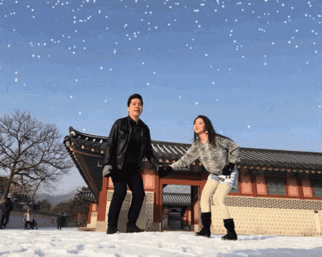 a man and a woman stand in the snow in front of a building