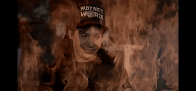 a man wearing a hat that says wayne 's world is surrounded by fire .