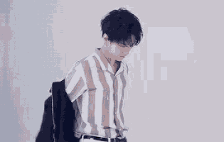 a young man wearing a striped shirt and a jacket is standing in front of a white wall .