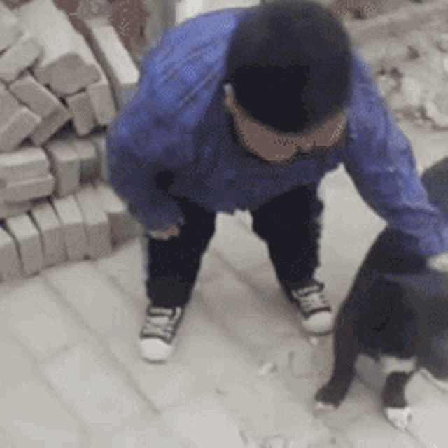 a man in a blue jacket is playing with a black dog