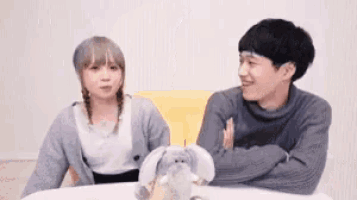 a man and a woman are sitting at a table with their arms crossed and a stuffed animal .