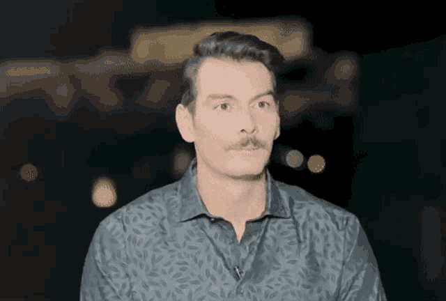 a man with a mustache is wearing a black shirt with a floral pattern