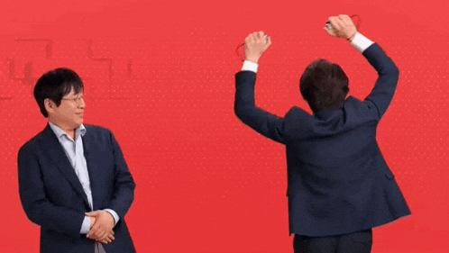 a man in a suit stands next to another man with his arms up