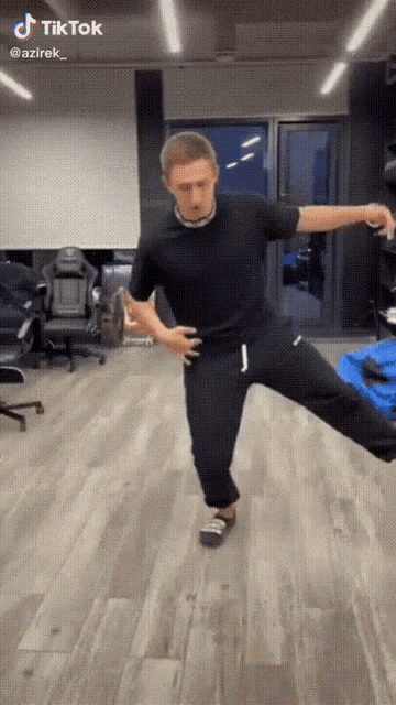 a man in a black shirt and black pants is dancing in a room with a blue bag in the background ..