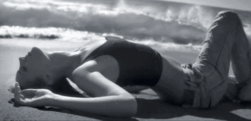 a black and white photo of a woman laying on the sand
