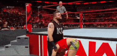 a wrestling match is taking place in a ring with a referee standing behind the ring .