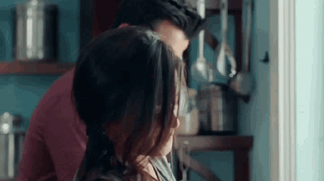 a man and a woman are kissing in the kitchen .