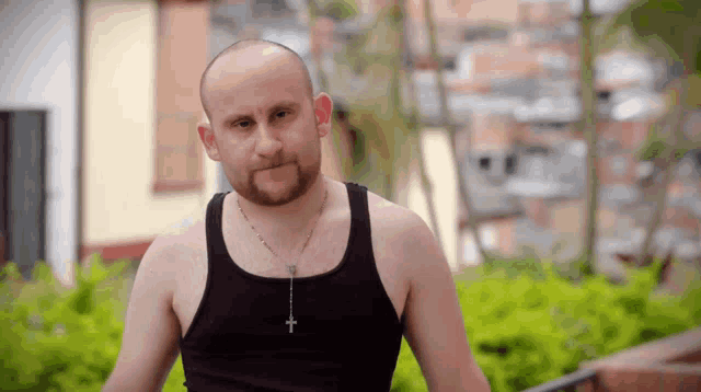 a bald man with a beard wearing a black tank top and a rosary around his neck