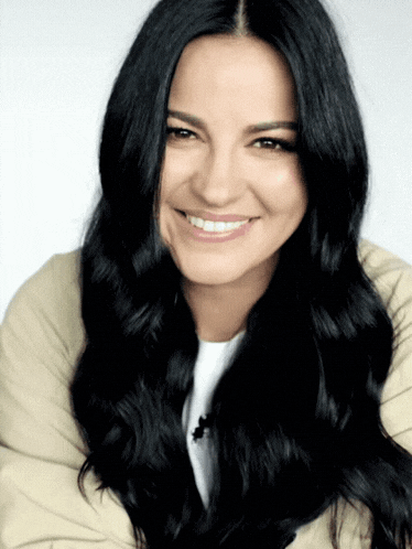 a woman with long black hair is smiling and wearing a white shirt