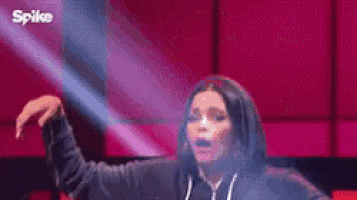 a woman in a hoodie is dancing on a stage in front of a pink wall .