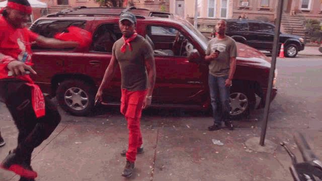a man with a bandana around his neck stands in front of a red car