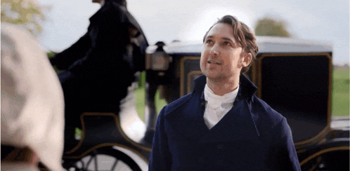 a man in a blue coat stands in front of a horse drawn carriage