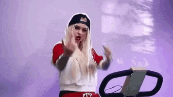a woman wearing a hat and a hoodie is riding a treadmill and giving the middle finger .
