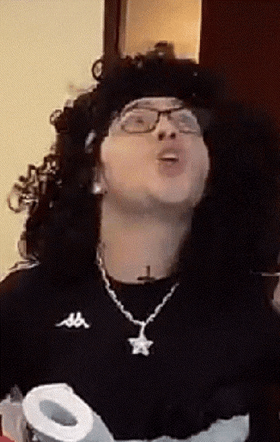 a man wearing glasses and a kappa sweater is blowing a kiss