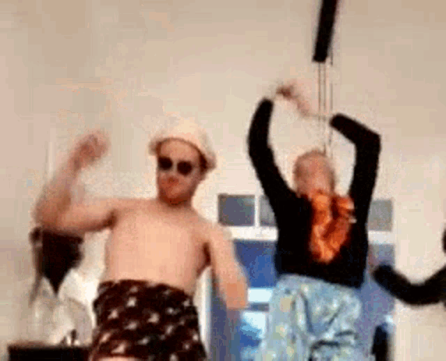 a man and a woman are dancing in a room . the man is wearing a hat and sunglasses .
