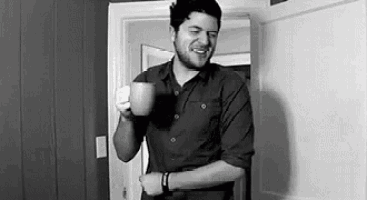 a man is standing in a doorway holding a cup of coffee and smiling .