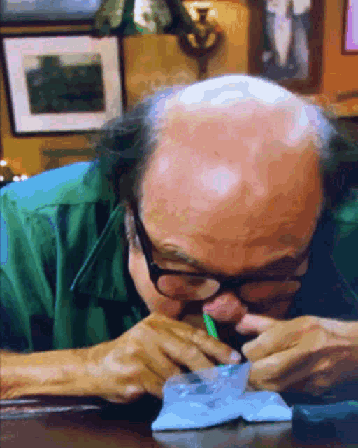 a bald man wearing glasses is sitting at a table with a pencil in his mouth