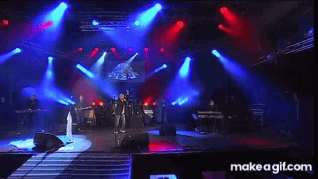 a man is singing into a microphone on a stage while a band plays instruments .