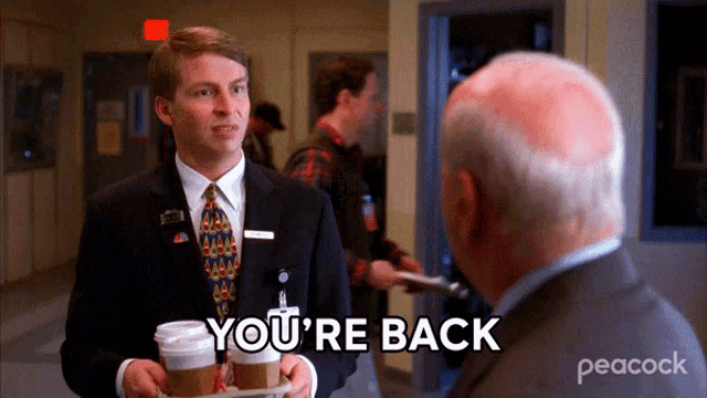 a man in a suit and tie talking to another man with the words " you 're back " on the screen