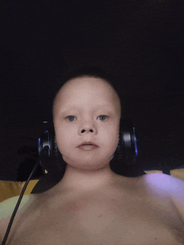 a shirtless child wearing headphones looks at the camera with a dark background